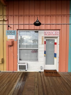 A brightly colored small building with a neon sign that reads "artxnikki"